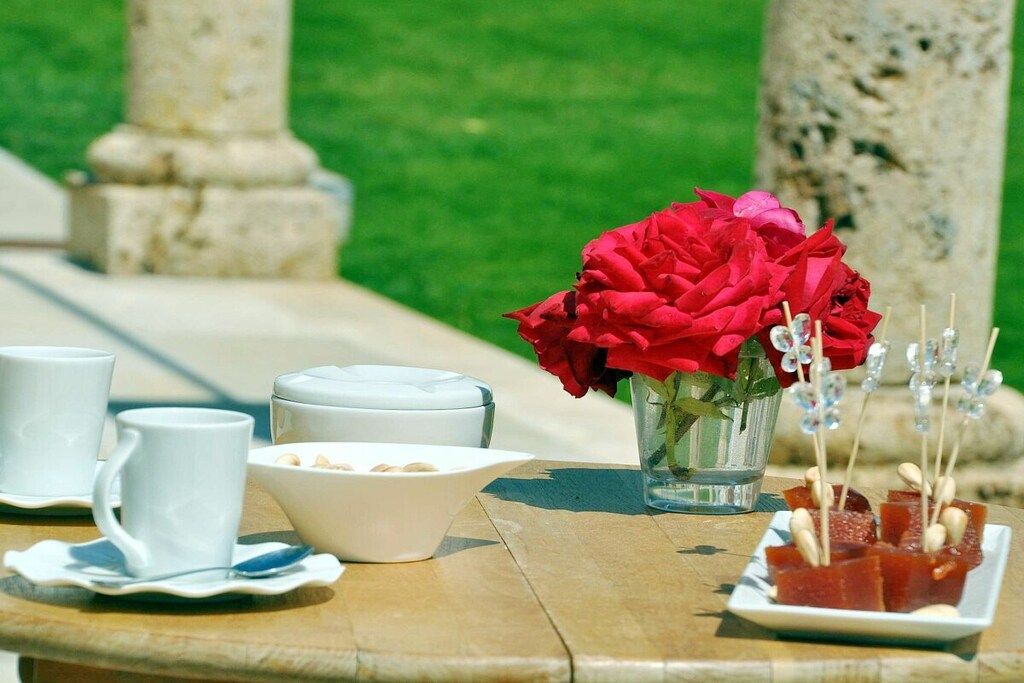 Uma mesa com uma tigela branca, um vaso de vidro com flores vermelhas e um prato com comida.