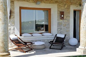 A stone building with a large window, two lounge chairs, and a round white object on the ground. - Ses Rentedores [2257] (Selva)