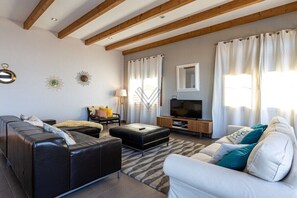 Un salon moderne avec un canapé, un pouf et un téléviseur posé sur un meuble en bois.