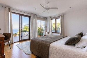 Een slaapkamer met een bed, een plafondventilator en uitzicht op de omgeving door een schuifdeur.