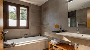 A modern bathroom with a bathtub, a vanity with a mirror, and a window. - SaTorre Voramar [4501A] (Sa Torre)