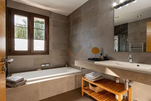 A modern bathroom with a bathtub, a vanity with a mirror, and a window. - SaTorre Voramar [4501A] (Sa Torre)