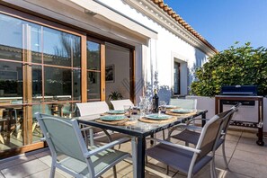 An outdoor dining area with a table set for four, surrounded by chairs, and a grill station to the side. - SaTorre Voramar [4501A] (Sa Torre)