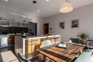A modern kitchen with a central island, a dining area with a wooden table, and a pendant light. - SaTorre Voramar [4501A] (Sa Torre)