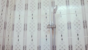 Une douche dotée d’un pommeau courbé et d’un système de douche à effet pluie vertical, dans une salle de bain dont les murs sont recouverts d’un papier peint à motifs.