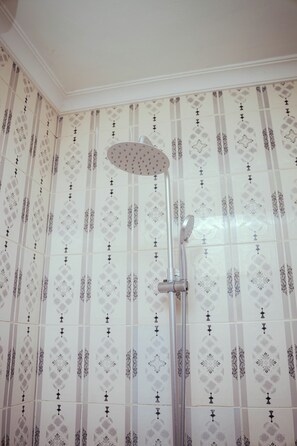 Ducha con cabezal curvo y ducha de lluvia vertical en un baño con papel tapiz estampado.
