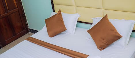 Una cama bien hecha con sábanas blancas, dos almohadas marrones y una toalla decorativa.