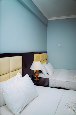 Habitación de hotel con dos camas individuales, una mesita de noche con lámpara y un interruptor de luz en la pared.