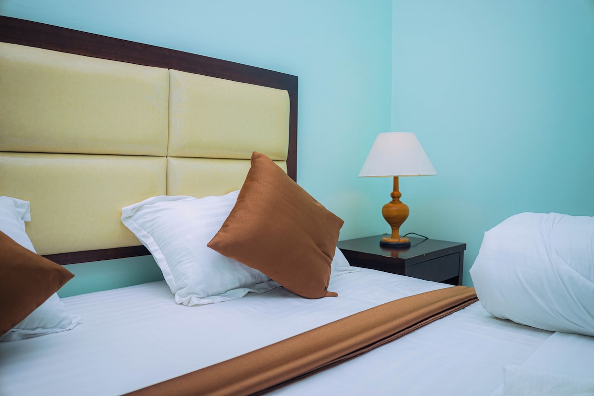 Una cama bien hecha con cabecera, lámpara de noche y almohadas.