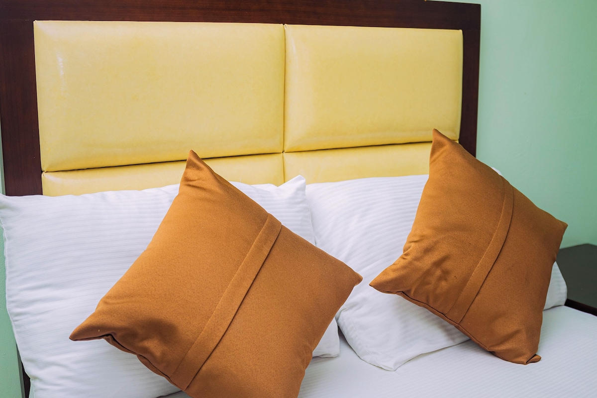 Una cama con cabecera, dos almohadas y una colcha blanca.