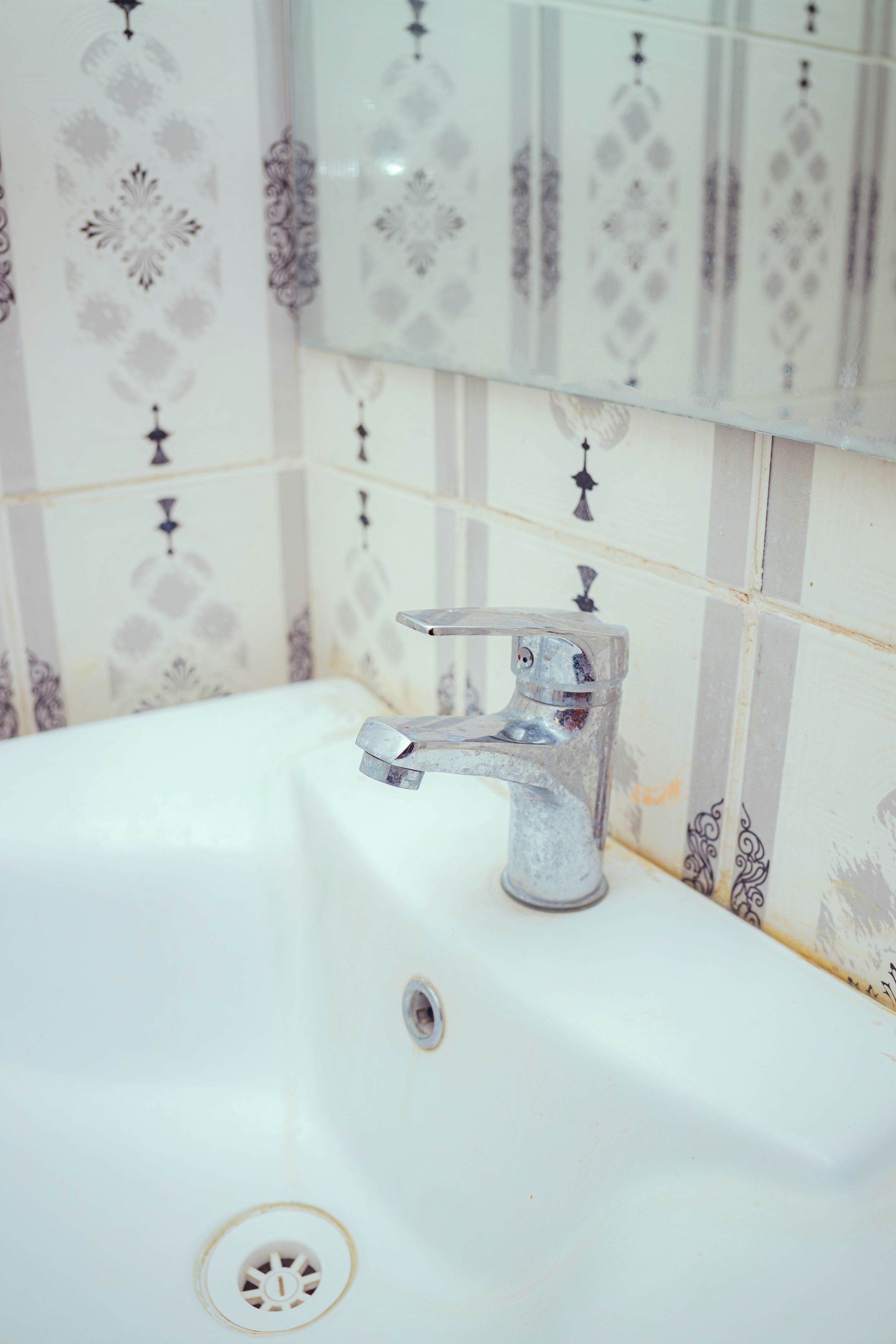 A bathroom with a white sink, a faucet, and patterned tiles on the wall.