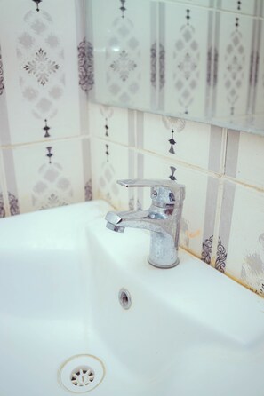 Un baño con lavamanos blanco, grifo y azulejos decorativos en la pared.