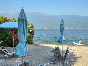 Uma área de estar à beira-mar com guarda-sóis, piscina e vista para o mar e montanhas.