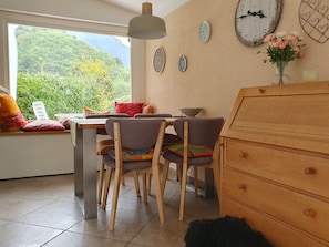 Uma área de refeições com vista para o verde, um armário de madeira e pratos decorativos na parede.