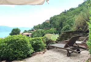Une terrasse avec une chaise en bois et une table, entourée de verdure et offrant une vue sur un paysage montagneux parsemé de maisons.