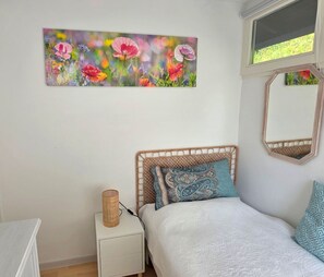 Une chambre à coucher avec un lit, une table de chevet, une lampe, un miroir et un tableau accroché au mur.