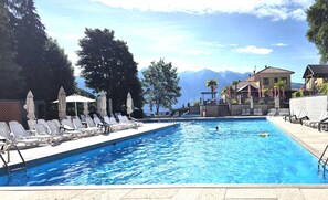 Une piscine avec des chaises longues et des parasols, une vue sur les montagnes et un bâtiment doté d’une terrasse.