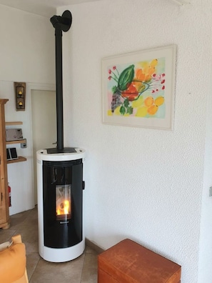 Une pièce avec un poêle à bois, un tableau floral encadré et un pouf marron.