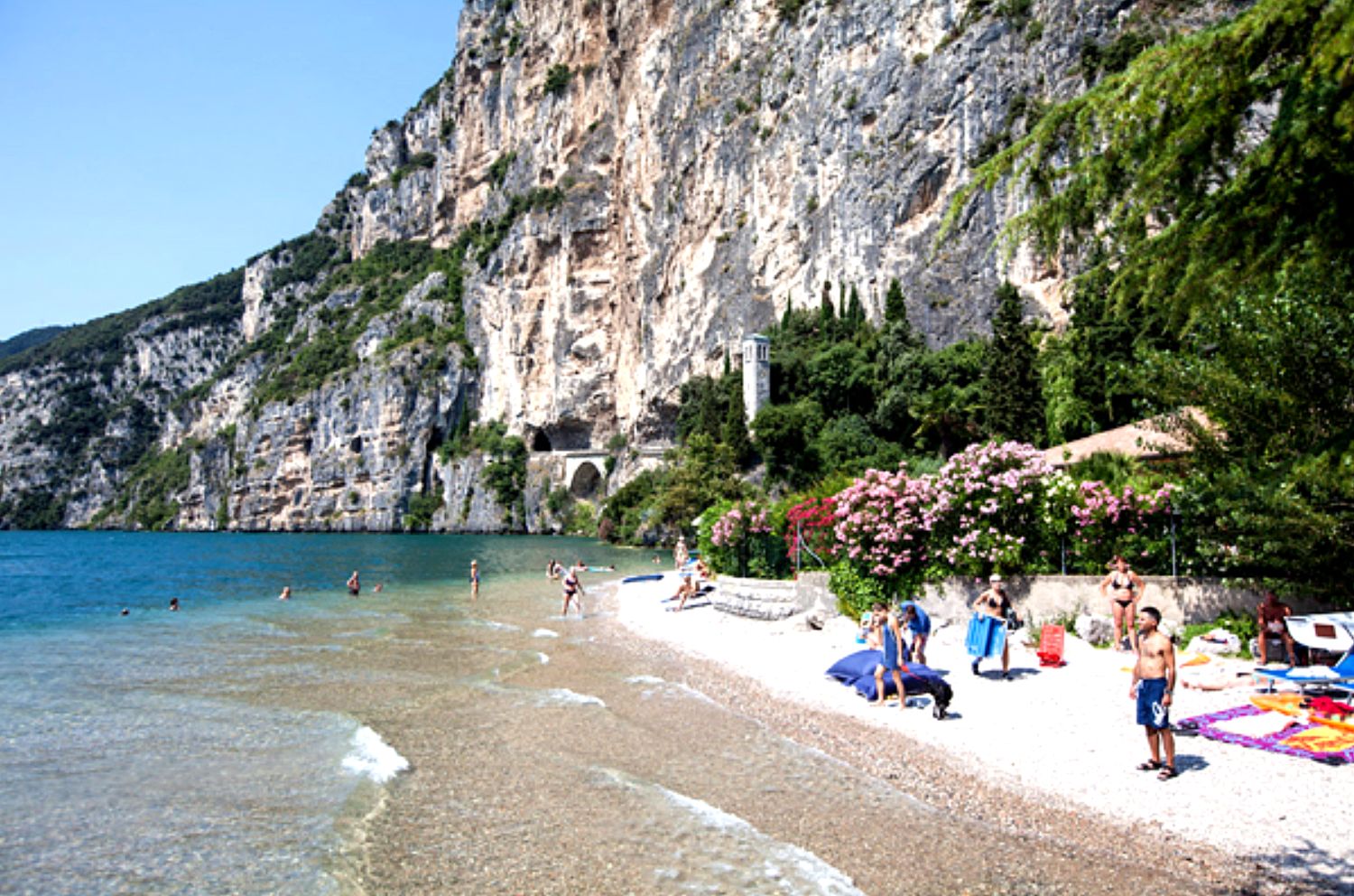 A beach with people, clear water, and rocky cliffs.