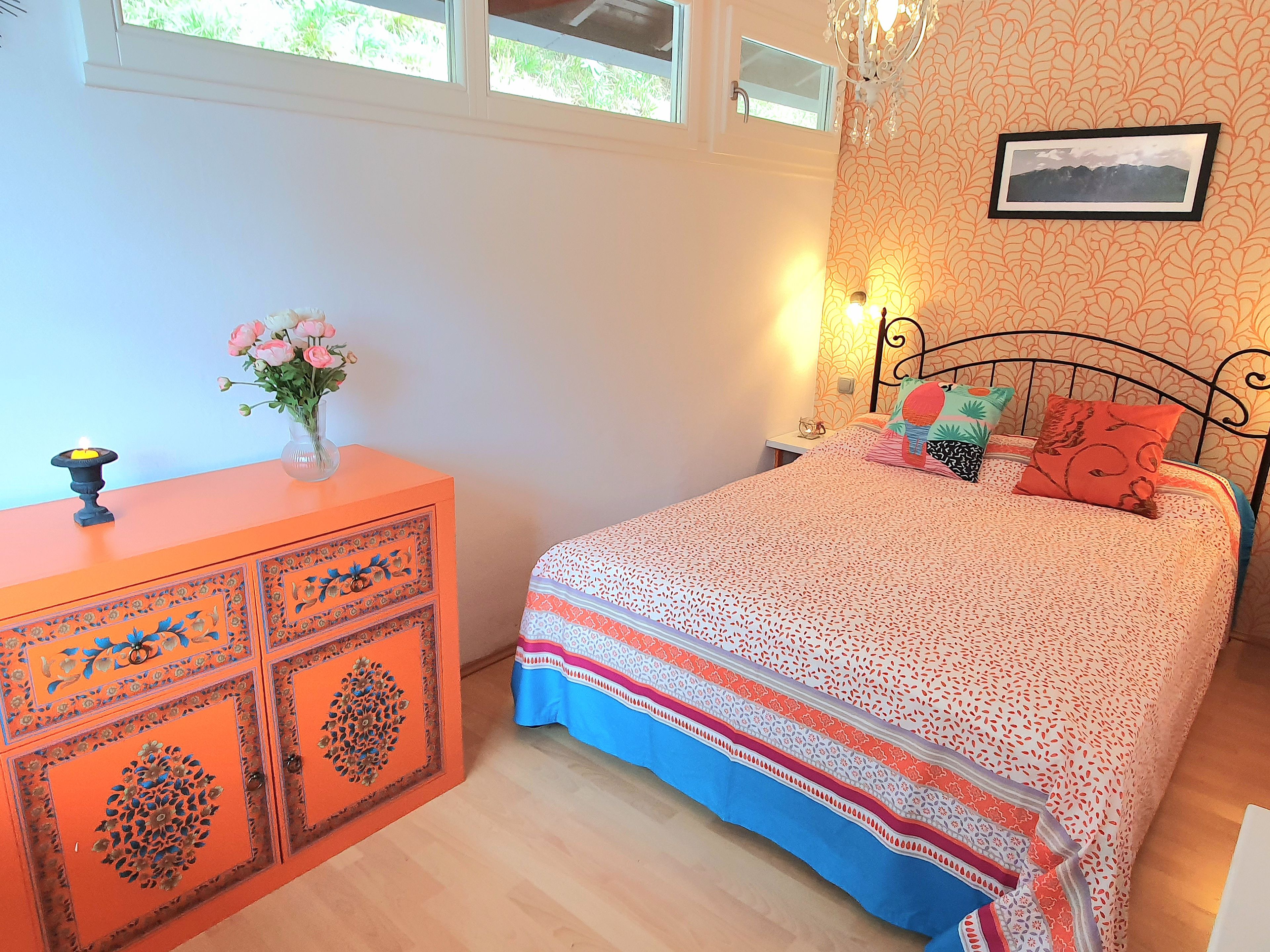 A bedroom with a bed, a dresser, a nightstand, a wall-mounted picture, and a window.