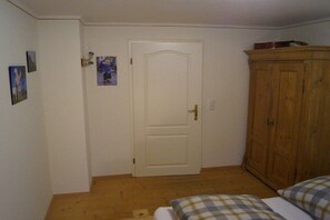 Une pièce avec une armoire en bois, un lit recouvert d’une couette à carreaux et une porte ornée d’un petit cadre.