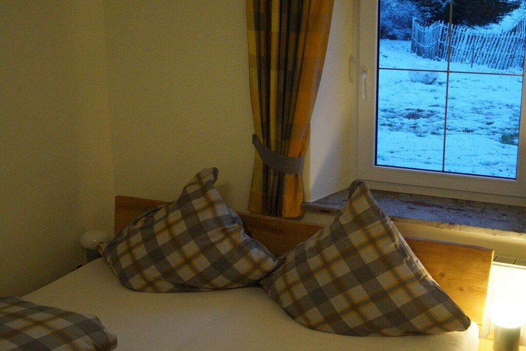 Cama com almofadas xadrez e janela com vista para paisagem nevada.