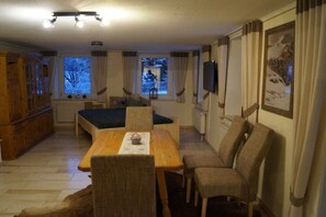 Habitació amb taula de dinar, cadires, sofà, televisió i finestres amb cortines.