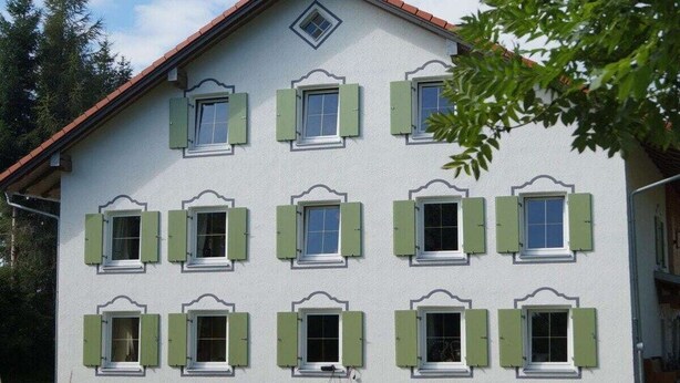 Un edificio de varios pisos con fachada simétrica, numerosas ventanas con contraventanas y un techo de tejas rojas.