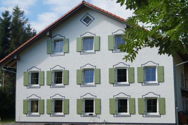 Un edifici de diverses plantes amb una façana simètrica, nombroses finestres amb persianes i un teulat de teules vermelles.