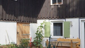 Una puerta de madera, una ventana con persiana verde y un banco de madera en un jardín.