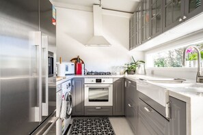A modern kitchen with stainless steel appliances, a built-in oven, and a window with a view of greenery. - Chiara`s Art Cottage 1BR Coastal Garden Retreat (Sorrento)