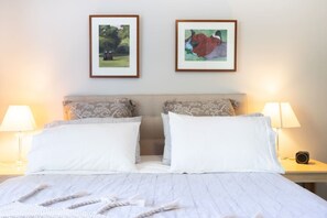 A double bed with white linens, two framed artworks above it, and bedside lamps on either side. - Chiara`s Art Cottage 1BR Coastal Garden Retreat (Sorrento)