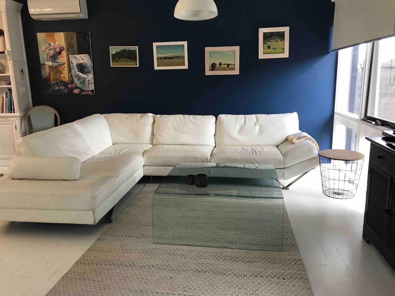 A modern living room with a white sectional sofa, a glass coffee table, and a large window providing natural light.