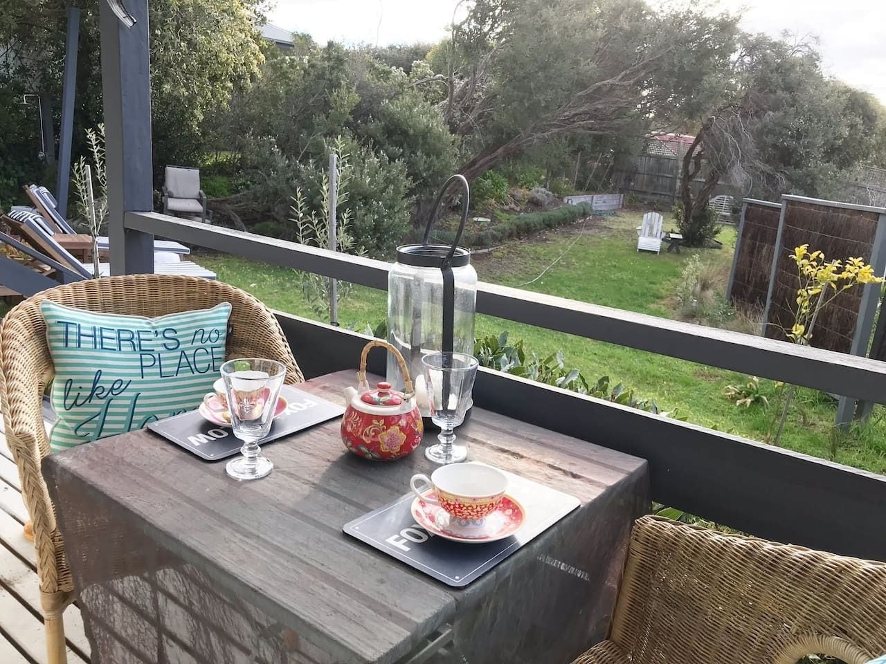 Una terraza de madera con una mesa preparada para tomar té, con una tetera, tazas y un tapete con un mensaje.