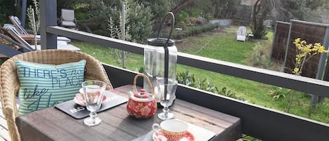 Un terrazzo in legno con un tavolo apparecchiato per il tè, che include un bollitore, tazze e un sottotavola con una scritta.