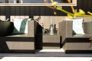 A wicker sofa set with cushions, a glass table, and a bottle.