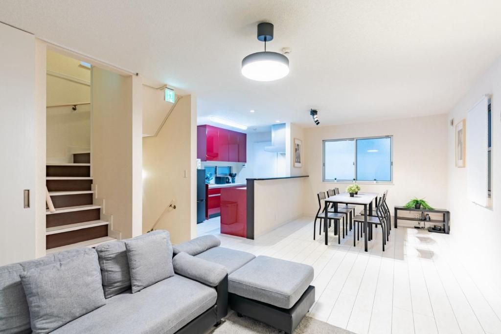 Una sala moderna con un sofá seccional gris, un comedor con mesa y sillas, y una cocina al fondo.