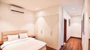 A bedroom with a bed, nightstands, a wardrobe, and an air conditioning unit.