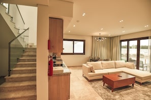A modern living room with a staircase, a large sectional sofa, a coffee table, and a dining area.