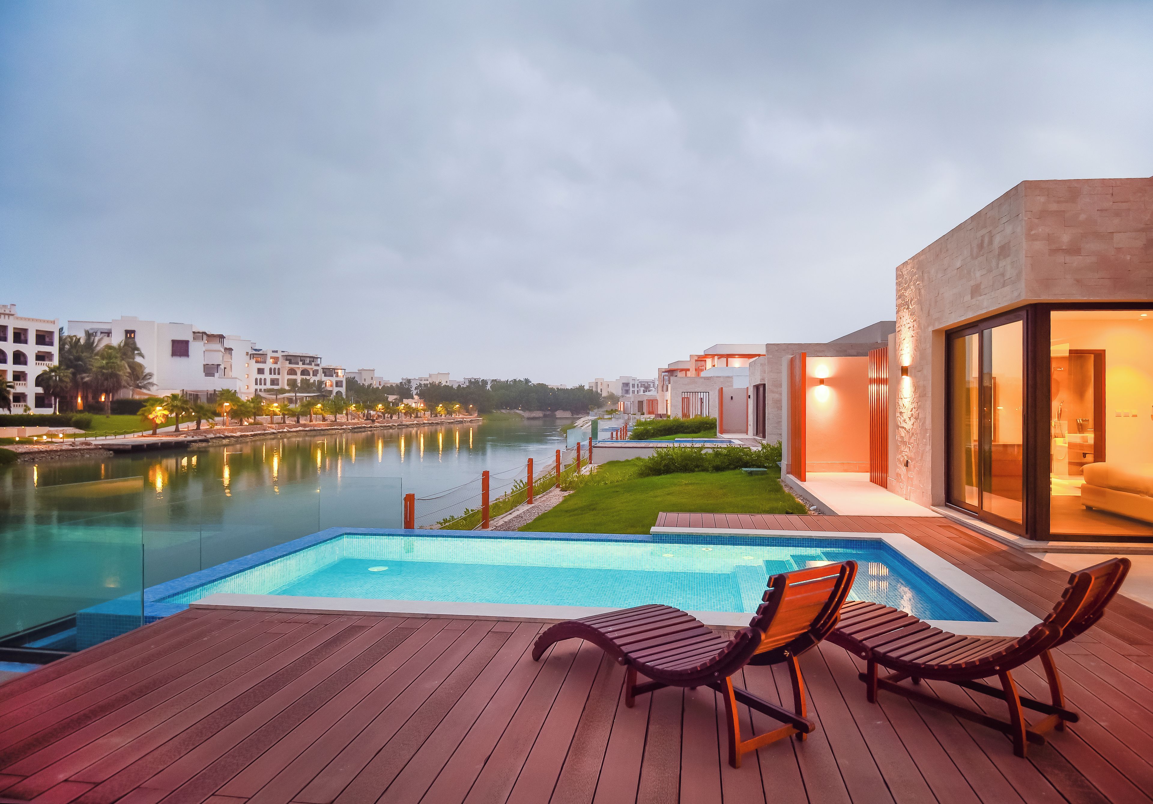 A swimming pool with lounge chairs, a river view, and modern buildings in the background.