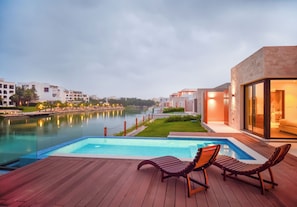A swimming pool with lounge chairs, a river view, and modern buildings in the background.
