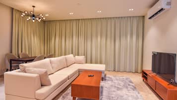 A modern living room with a sectional sofa, a wooden coffee table, a TV on a stand, and a ceiling light fixture.