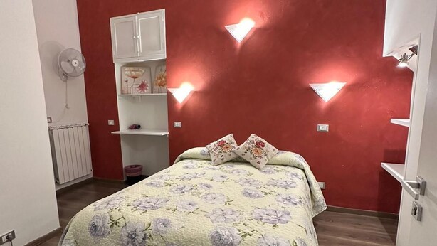 Un dormitorio con una cama, un armario blanco, un radiador y un ventilador de pared.