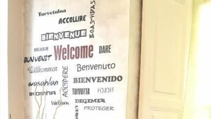Una pared con un letrero que dice 'Welcome' y una silla con un cojín floral.