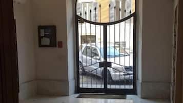 Ein Flur mit poliertem Boden, einem schwarzen Tor und Blick auf geparkte Autos vor dem Haus.