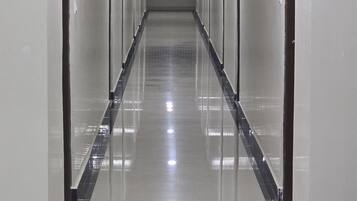 A long, narrow hallway with doors on both sides, a tiled floor, and a ceiling with recessed lighting.