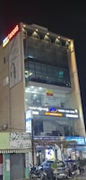 Un edificio de varios pisos con señalización que indica 'KONTOURA VISION' y 'Vasan Eye Care' a nivel de calle.