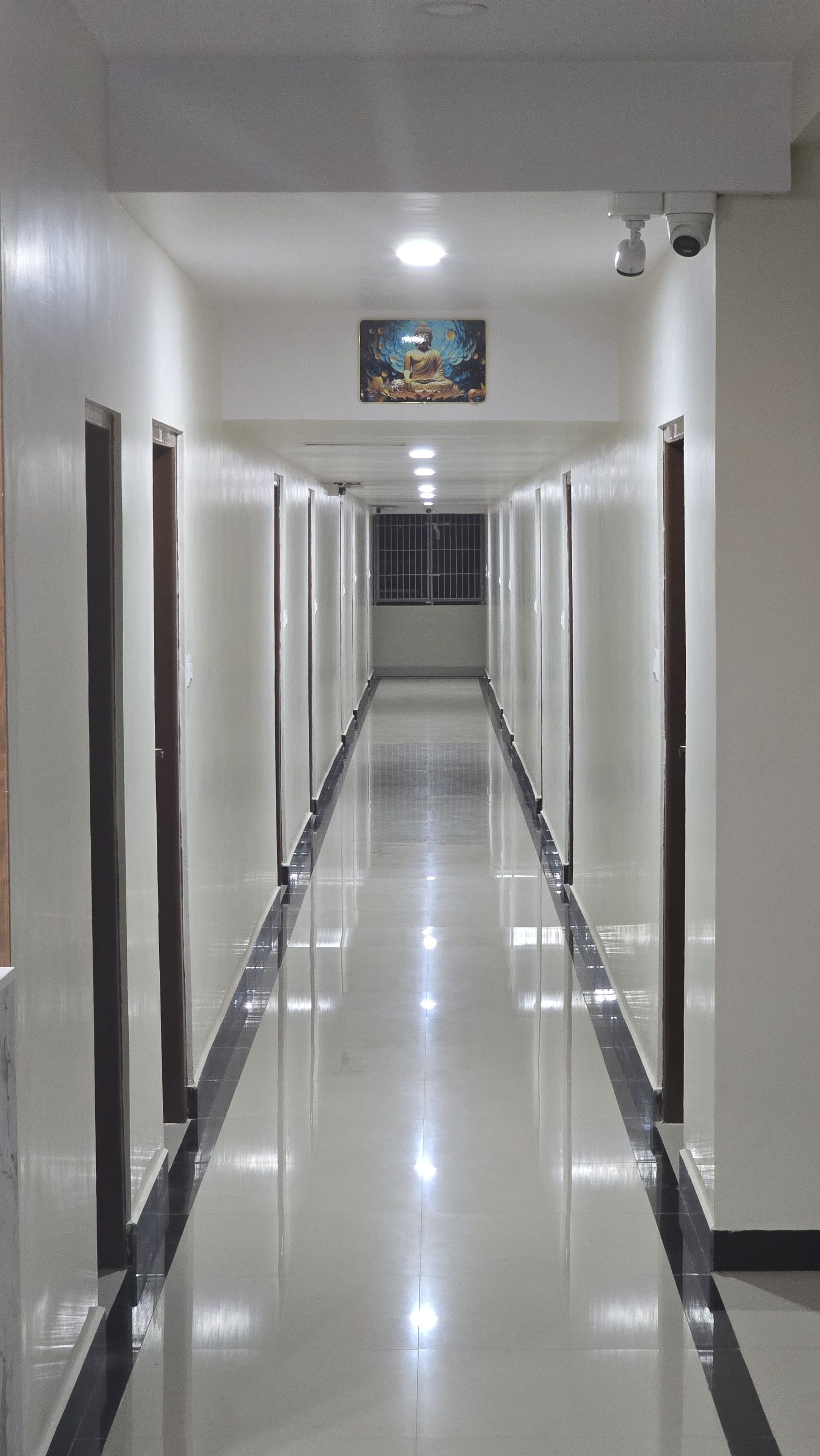 A long, narrow hallway with doors on both sides, a tiled floor, and a ceiling-mounted security camera.