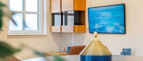 Una habitación con una mesa redonda, una ventana, un estante en la pared y un cuadro.