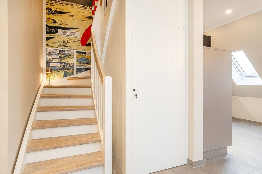 A staircase with wooden steps leading to a white door, a skylight, and a wall with comic strip panels.
